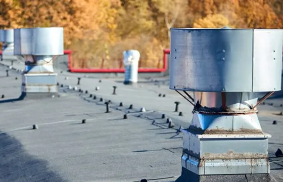 Commercial chimney setups on a flat roof, showing vents and colorful fall trees in the background.