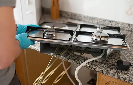 Person wearing gloves working on a kitchen gas stove installation or repair.